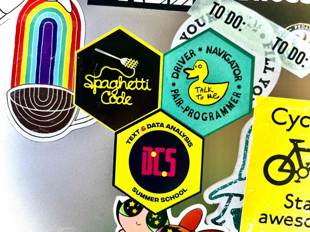 laptop stickers from the summer school, including the pair-programming proficiency badge